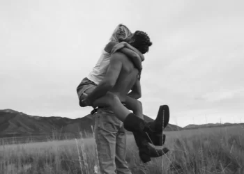 Man lifting a woman in a joyful embrace in a field, exemplifying the use of 'motion blur lightroom presets' in black and white photography.