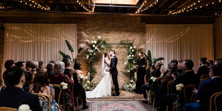 Bride and groom kiss under skylight and boho floral arch at their spring Arbory wedding in Chicago