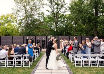 Bride and groom kiss in aisle while guests cheer after their garden wedding ceremony at Warehouse 109 in Plainfield, Illinois